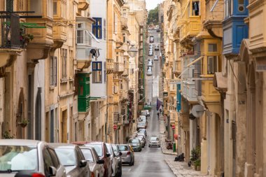 Valletta, Malta 26 Haziran 2021: Valletta, Malta 'da geleneksel Malta balkonlarının yer aldığı arabalar ve tarihi evlerle dolu dar bir cadde.