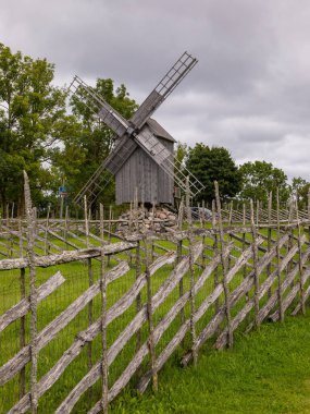 Saaremaa, Estonya - 24 Ağustos 2021: Taştan bir üsteki geleneksel ahşap yel değirmeni kırsal kesimde ahşap bir çitle çevrili duruyor.