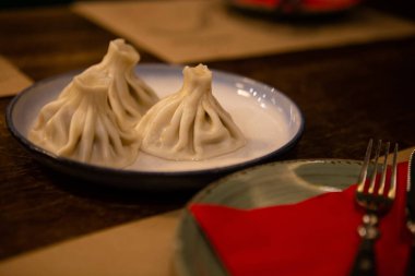 Geleneksel haşlanmış hamur köfteleri servis masasında. Restoranda et, peynir, çatal ve tabakla geleneksel Gürcü yemekleri. Lezzetli yemek, Gürcü mutfağı..