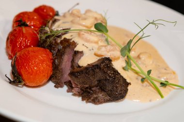 Fırında domates, kızarmış biftek ve beyaz tabakta karides sosu. İtalyan restoranında akşam yemeği. İtalyan aşçısından özel yemek..