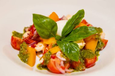 Beyaz tabakta pesto ve fesleğen yapraklarıyla servis edilen salata Caprese. Domatesli salata, caprese, fesleğen ve pesto. İtalyan mutfağı konsepti, vejetaryen yemekleri.