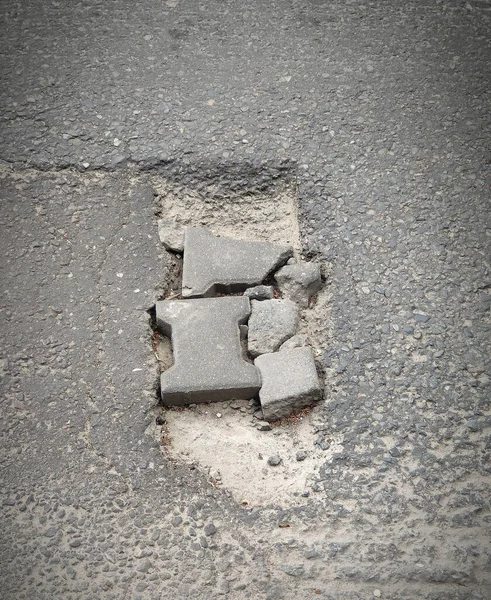 Cracked road, street with pothole, top view. Large pit with stones on the asphalt road, gray color. Damaged street surface.