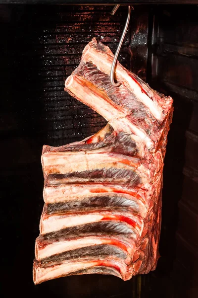 Row ribs hanging on a hook, fresh meat. Meat on bones, ready for preparing in restaurant. Manufacturing of meat concept, meat ribs in a fridge, pig or cow meat for food. Fresh pig ribs.