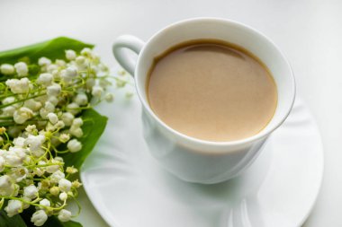 Kahve fincanı ve bir buket çiçekli vadi zambağı. Yukarıdan bakıldığında, sabah vakti konsepti, çiçeklerle süslenmiş süsler..