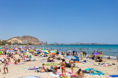 5 Temmuz 2023 Postiguet plajı Alicante, Costa Blanca sahilinde güneşlenen insanlar. Yaz zamanı, deniz tatil köyü, mavi gökyüzü, arka planda dağ.