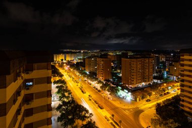 ALICANTE, İSPAN - Eylül 2023: Alicante, İspanya 'da hava manzaralı cadde, gece vakti. Palmiye ağaçları ve arabalarla dolu bir yol, gece fotoğrafları. Şehir manzarası, ışıklar, modern binalar..
