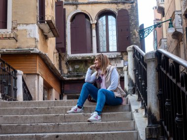 Relaxed tourist woman sitting on the stairs on a bridge in the city of Venice, Italy. Tourism concept.