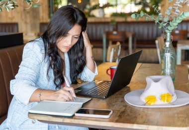 Bir kafede dizüstü bilgisayarla çalışan bir kadın notlar okuyor. Teknoloji ve iş konsepti.