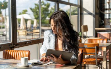 Bir kafede çalışırken dijital tablet ve cep telefonu kullanan bir kadın. Teknoloji ve iş konsepti.