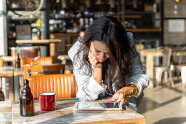 Kahve dükkanında masaya yaslanırken dijital tablet kullanan bir kadın. Teknoloji konsepti.