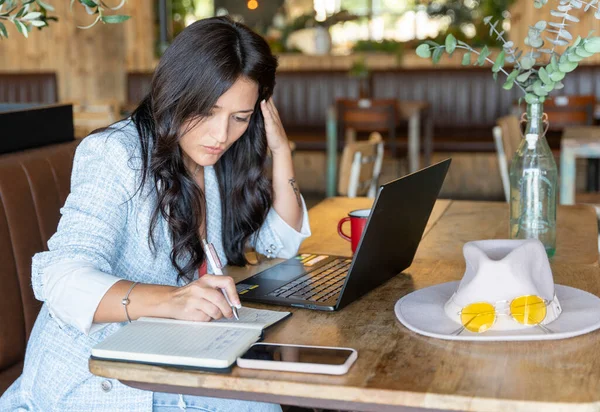 Bir kafede dizüstü bilgisayarla çalışan bir kadın notlar okuyor. Teknoloji ve iş konsepti.