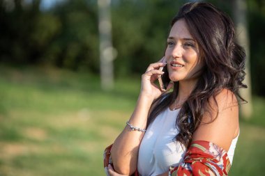 Güneşli bir günde doğada ayakta dikilen bir kadın telefonda konuşuyor. Teknoloji konsepti.