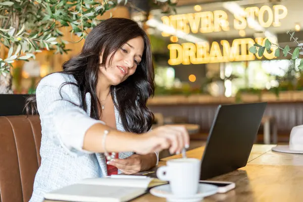 Woman stirring a coffee while working sitting in the coffee shop. Technology and business concept.