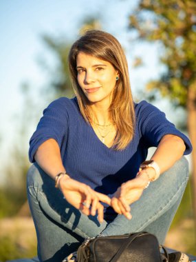 Gün batımında parkta oturmuş kameraya bakan rahat bir kadın..