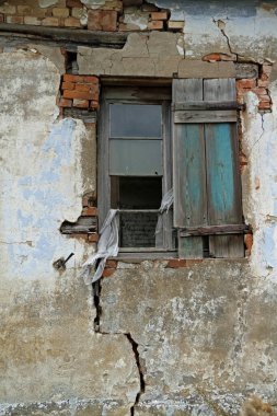 Harap olmuş kepenkleri ve harap olmuş, çökmüş bir duvarı olan kırık bir pencere.
