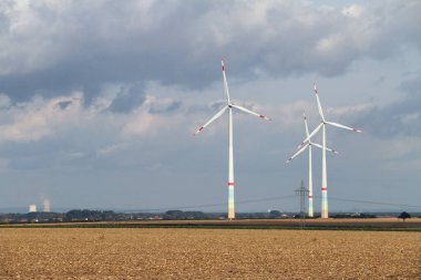 Arka planda bulutlu bir gökyüzü olan açık bir alanda birkaç rüzgar türbini.