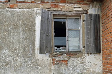 Harap olmuş kepenkleri ve harap olmuş, çökmüş bir duvarı olan kırık bir pencere.