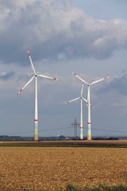 Arka planda bulutlu bir gökyüzü olan açık bir alanda birkaç rüzgar türbini.