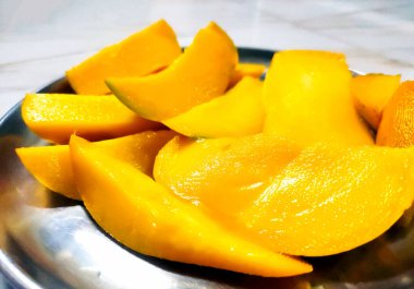 Geleneksel çelik tabakta servis edilen altın sarısı mango dilimleri.
