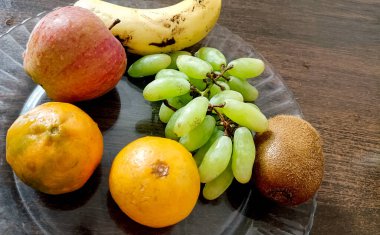Görüntü, ahşap bir yüzey üzerinde şeffaf bir cam plaka üzerinde düzgün bir şekilde yerleştirilmiş taze meyve çeşitlerini gösteriyor.