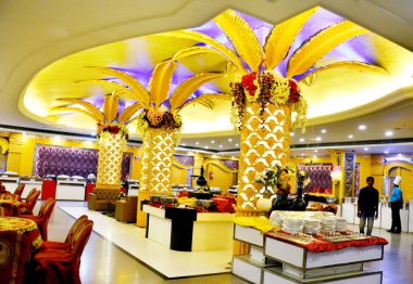 Hisar, Haryana, 10 Ağustos 2025: Zarif bir şölen salonu iç mimarisi, çiçek süslemeli yuvarlak masalar ve servis için hazır büfe tezgahı, düğünler ve etkinlikler için ideal.