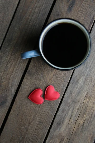 Two red hearts and a cup of coffee on a wooden background.