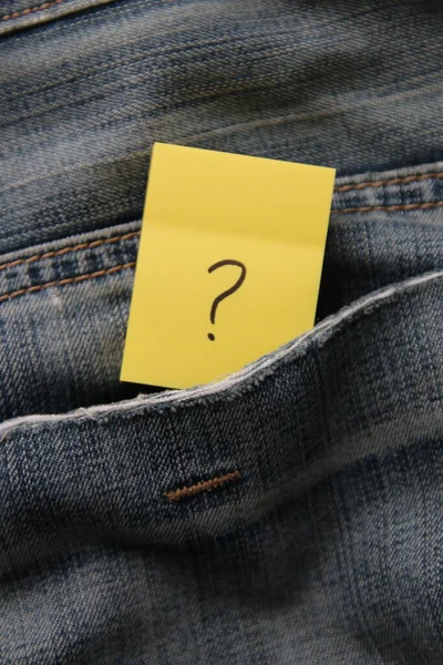A question mark on a paper tag in a jeans pocket. Question mark on jeans.