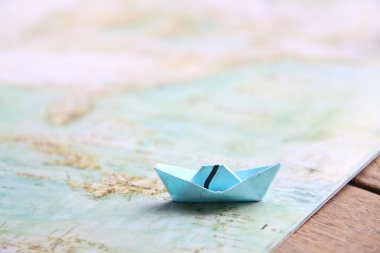 Paper boat on vintage map and wooden background.