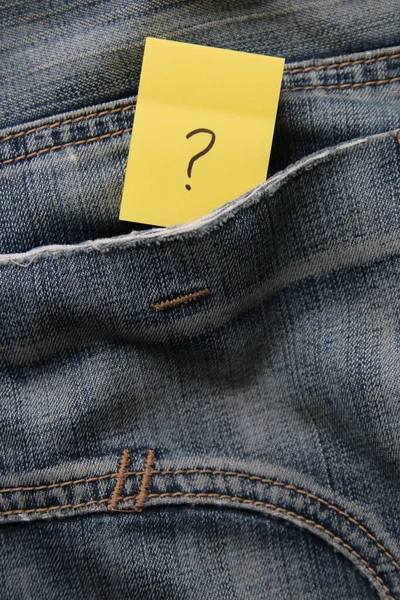 A question mark on a paper tag in a jeans pocket. Question mark on jeans.