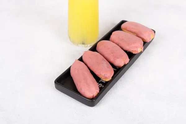 Açık mavi dikdörtgen bir plaka üzerinde dairesel desenli altı adet pembe Clair yakın plan. Clair 'lerin parlak bir kapanışı var ve mükemmel bir şekilde hizalanmışlar. Resim yukarıdan aşağıya doğru çekiliyor, hamur işlerinin canlı rengini vurguluyor.