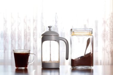 Taze demlenmiş kahve, French Press ve Ground Coffee kavanozu ahşap masa ev kahvesi üzerine.