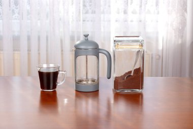 Taze demlenmiş kahve, French Press ve Ground Coffee kavanozu ahşap masa ev kahvesi üzerine.