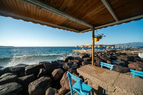 Geleneksel Akdeniz Sahil Restoranı Mavi Tahta Sandalyeler ve Deniz Kenarı Terasında Kırmızı Kareli Masa örtüleri Yaz boyunca Rocky Coast manzaralı