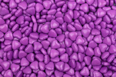 Pürüzsüz bir arkaplan oluşturan parlak yüzeyli mor kalp şeklinde şekerler. Sevgililer Günü, aşk ve romantizm temaları için mükemmel bir şekerleme dokusu..