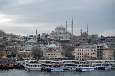 03.13.2025, İstanbul, Türkiye. Tarihi bir cami ve minarelerle çarpıcı bir şehir manzarası. Gökyüzü bulutlu ve dramatik bulutlu, rıhtımlı tekneleri olan canlı bir rıhtım manzarası..