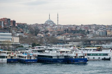 03.13.2025, İstanbul, Türkiye. Tarihi bir cami ve minarelerle çarpıcı bir şehir manzarası. Gökyüzü bulutlu ve dramatik bulutlu, rıhtımlı tekneleri olan canlı bir rıhtım manzarası..