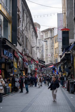 03.13.2025, İstanbul, Türkiye. Canlı dükkanlar, renkli işaretler ve neşeli ışıklarla dolu tarihi bir pazarda hareketli bir cadde bulutlu bir gökyüzü altında canlı şehir atmosferini yakalıyor.. 