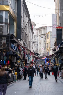 03.13.2025, İstanbul, Türkiye. Canlı dükkanlar, renkli işaretler ve neşeli ışıklarla dolu tarihi bir pazarda hareketli bir cadde bulutlu bir gökyüzü altında canlı şehir atmosferini yakalıyor.. 
