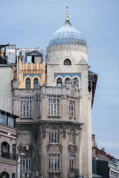 Tarihi mimarinin cazibesini, kubbeli bir kule, dekoratif pencereler ve şenlikli dizaynla süslenmiş sakin bir gökyüzüne karşı şenlikli ışıklarla süslenmiş geleneksel bir binanın çarpıcı görüntüsüyle keşfedin.. 