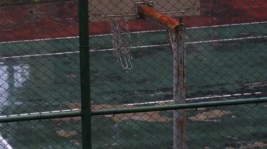 Rusty Basketball Hoop in the Rain with Swaying Net and Raindrops Falling on Wet Court - Terk Edilmiş Açık Hava Spor Alanında Rüzgarlı Bir Gün
