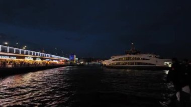 Geceleri Galata Köprüsü altındaki restoranlar. İstanbul Sahil Kıyısı Deniz Ürünleri Mekanları ve Boğaz Yansımaları ile Akşam Yemeği - Tarihi Köprü boyunca Türk Gece Hayatı Sahnesi. İnsanlar yemeklerini deniz manzaralı yiyorlar..