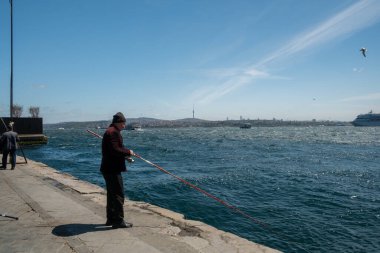 04.28.2025, İstanbul, Türkiye. Türkiye 'de Açık Gök Altında Dalgalı Mavi Su ve Köprü Manzaralı İstanbul' da Boğaz Kıyısında Balıkçılar.
