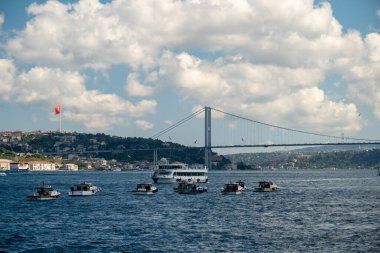 05.14.2025, İstanbul, Türkiye. İstanbul, Türkiye 'deki Boğaz Köprüsü' nün altından geçen büyük gemilerle İstanbul 'da balıkçı tekneleri manzaralı bulutlar ve arka planda tepelerle aydınlık bir günde.