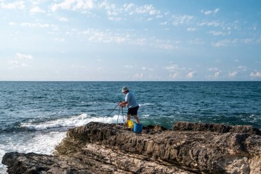 Güneşli bir günde açık mavi gökyüzü ve okyanus dalgalarıyla kayalık sahil şeridinde balıkçılık - açık hava eğlencesi ve deniz aktivitesi