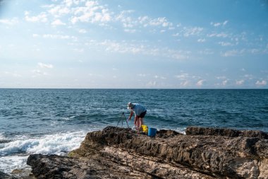 Güneşli bir günde açık mavi gökyüzü ve okyanus dalgalarıyla kayalık sahil şeridinde balıkçılık - açık hava eğlencesi ve deniz aktivitesi