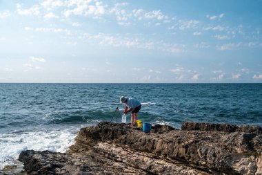 Güneşli bir günde açık mavi gökyüzü ve okyanus dalgalarıyla kayalık sahil şeridinde balıkçılık - açık hava eğlencesi ve deniz aktivitesi