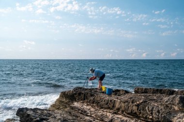 Güneşli bir günde açık mavi gökyüzü ve okyanus dalgalarıyla kayalık sahil şeridinde balıkçılık - açık hava eğlencesi ve deniz aktivitesi