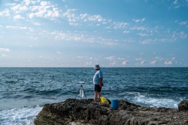 Güneşli bir günde açık mavi gökyüzü ve okyanus dalgalarıyla kayalık sahil şeridinde balıkçılık - açık hava eğlencesi ve deniz aktivitesi