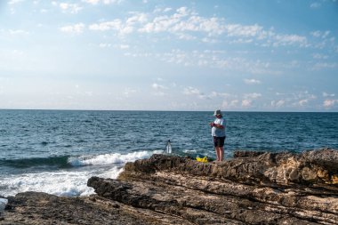 Güneşli bir günde açık mavi gökyüzü ve okyanus dalgalarıyla kayalık sahil şeridinde balıkçılık - açık hava eğlencesi ve deniz aktivitesi