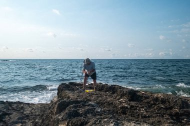 Güneşli bir günde açık mavi gökyüzü ve okyanus dalgalarıyla kayalık sahil şeridinde balıkçılık - açık hava eğlencesi ve deniz aktivitesi